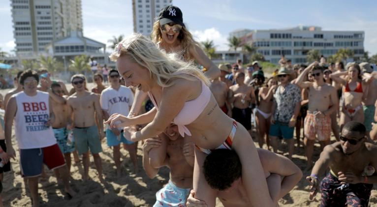 Cece Guida, de 19 años y procedente de la ciudad de Nueva York, sobra Sam Reddick, de 20 años y procedente de Evansville, Indiana, durante un juego organizado durante las vacaciones de primavera en una playa el 17 de marzo de 2020 en Pompano Beach, Florida. (AP Foto/Julio Cortez)