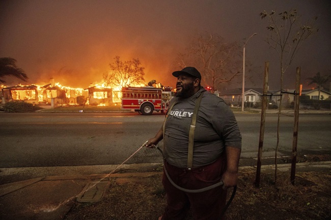 Un vecino de Eaton intenta sofocar las llamas en su propiedad con una manguera de jardín. Foto: Ethan Swope / AP.