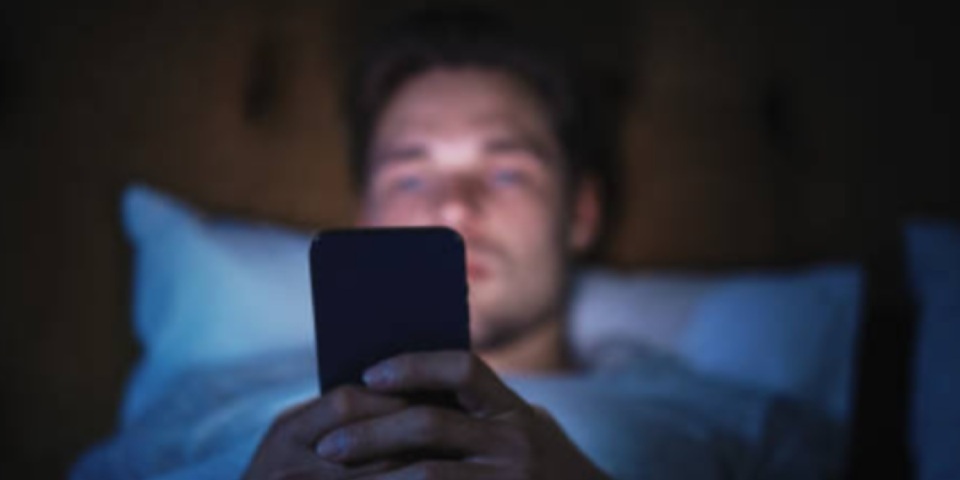 Joven en cama revisando celular