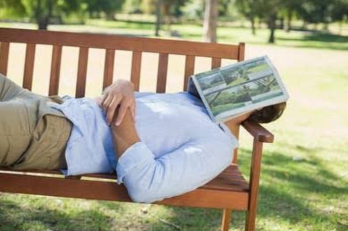 Young man sleeping on a bench with his face covered by a book