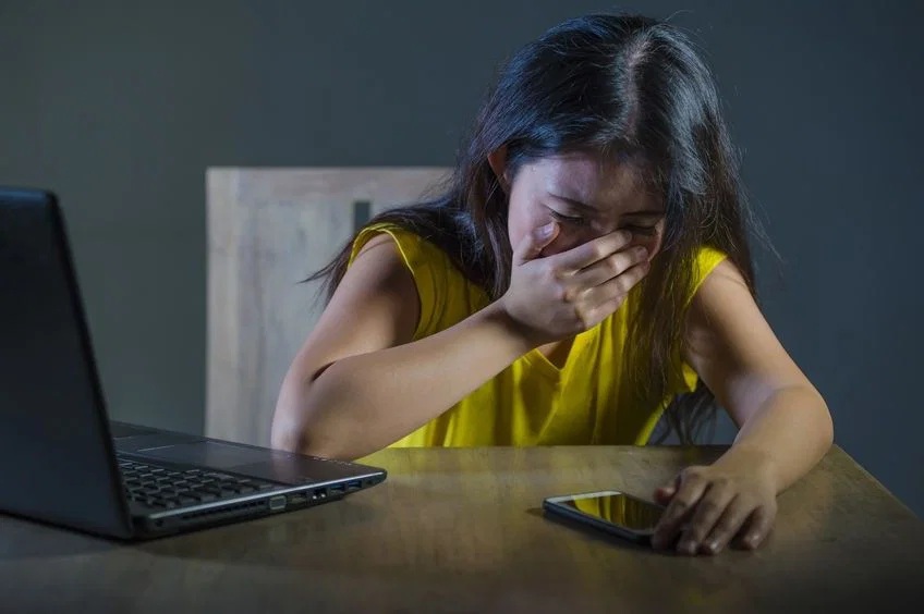 Adolescent victim of cyberbullying crying in front of a screen
