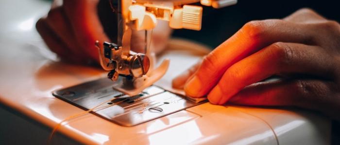 Manos de mujer ensartando aguja de máquina de coser.